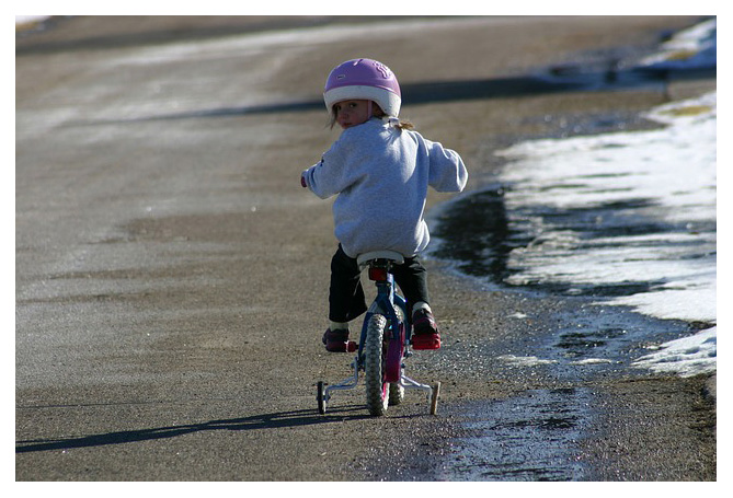 girl riding a bike with training wheels